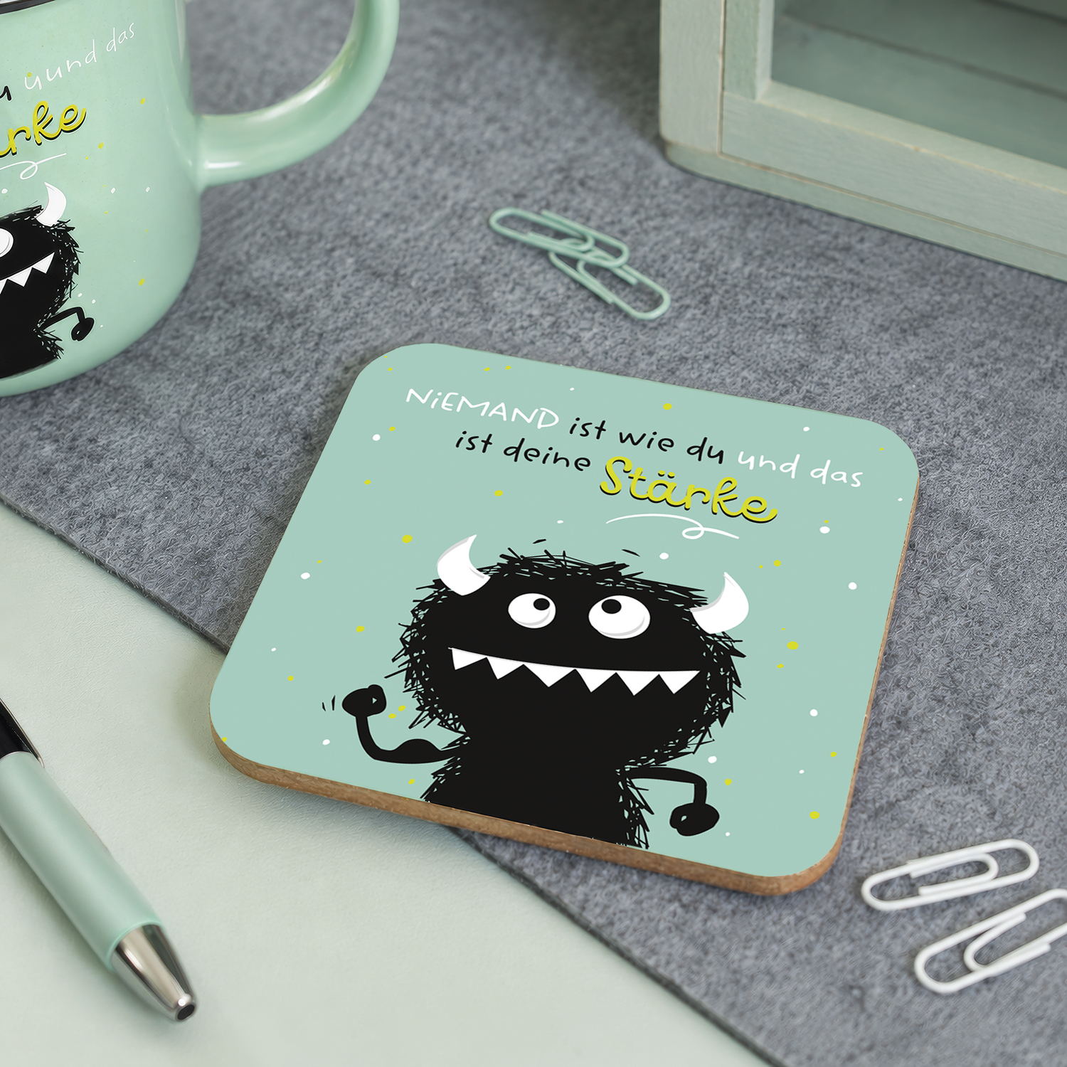 Mintgrüner Untersetzer mit schwarzem Monster-Motiv und gelbem Schriftzug Stärke