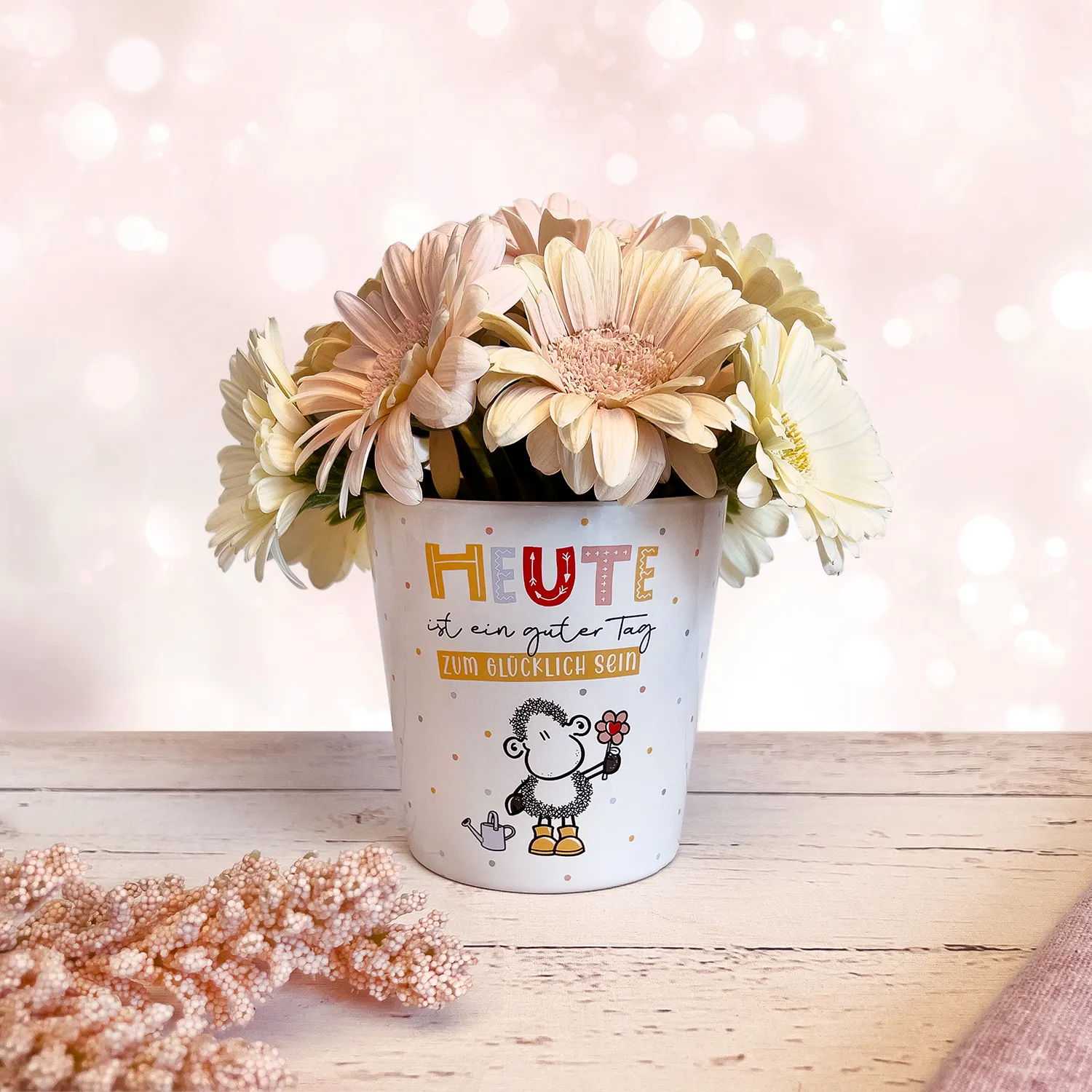 Weißer Steinzeug-Übertopf mit Schäfchen-Motiv und Blumen-Print auf hellem Holztisch