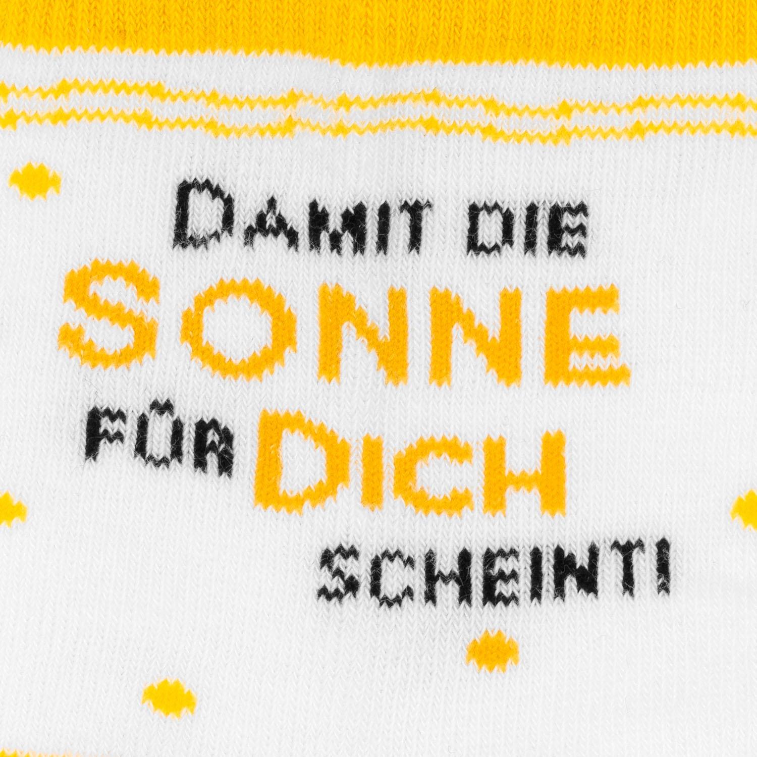 Weiße Zaubersocken mit gelben Sonnenmotiven und schwarzem Text.