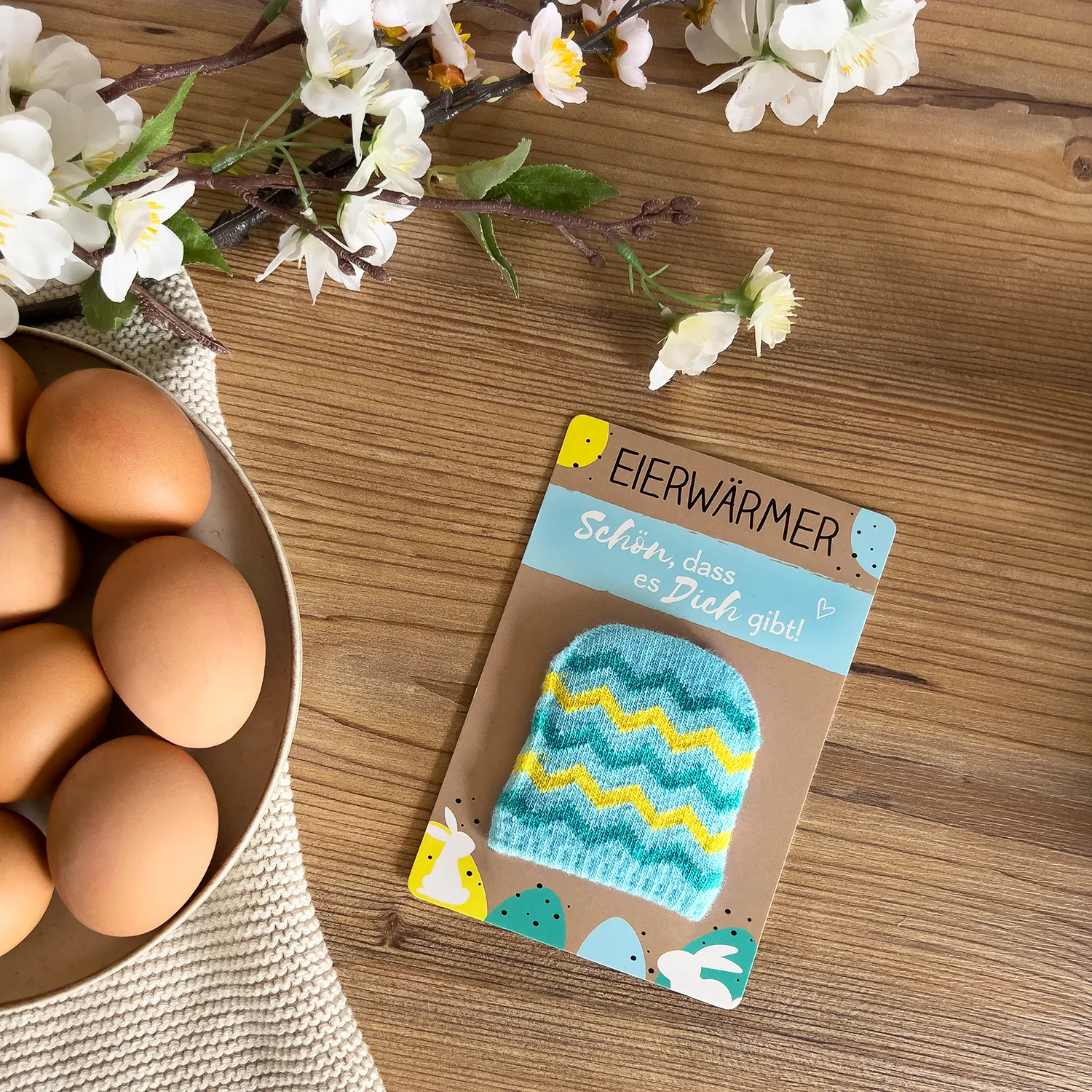 Flauschiger türkiser Eierwärmer mit gelben Zickzackstreifen auf Headercard