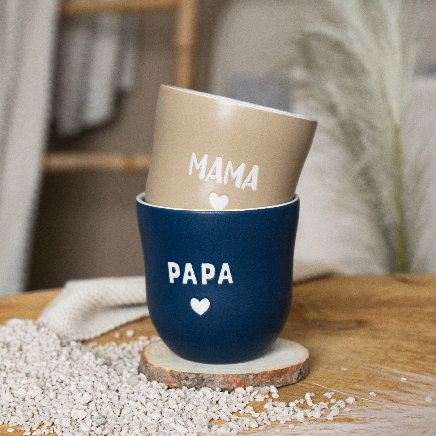 Lieblingsbecher Papa in Marineblau mit Herz; beige Becher Mama daneben, auf Holzunterlage