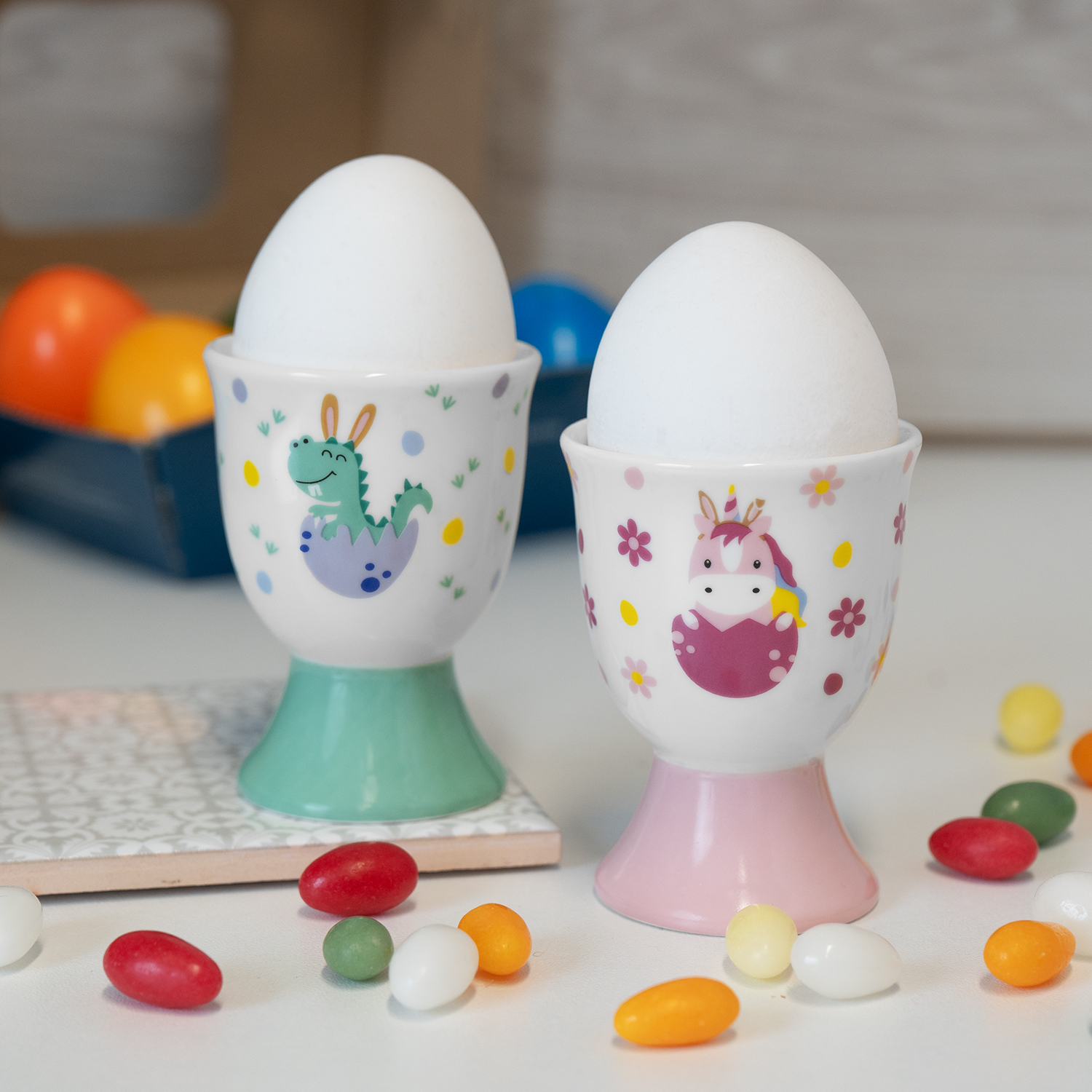 Zwei Porzellan-Eierbecher mit Einhorn- und Drachenmotiv auf pastellfarbenen Füßen.