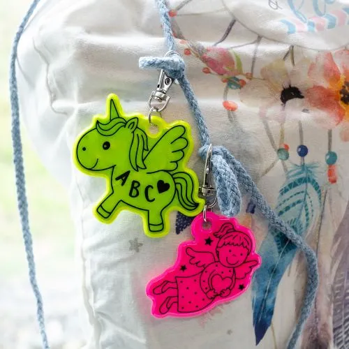 Ein Neon-Reflektor mit Einhorn-Motiv und ein Neon-Reflektor mit Engel-Motiv, angebracht an einem Turnbeutel.