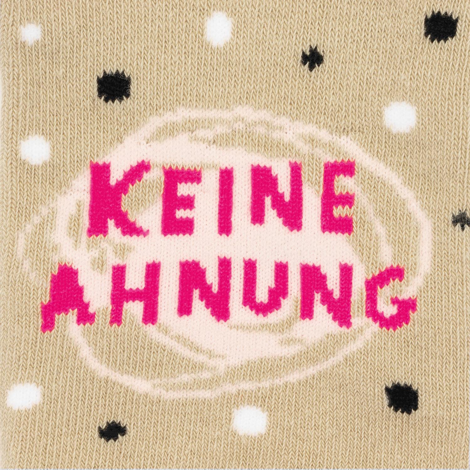 Beige gestrickte Zaubersocken mit pinkem Schriftzug 'KEINE AHNUNG' und Punktmuster