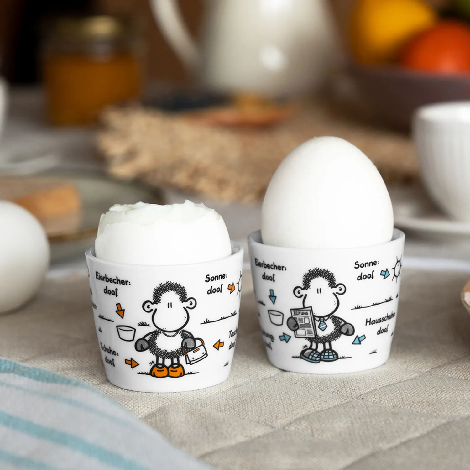 Zwei weiße Porzellan-Eierbecher mit Schäfchen-Motiv, je ein Ei darauf.