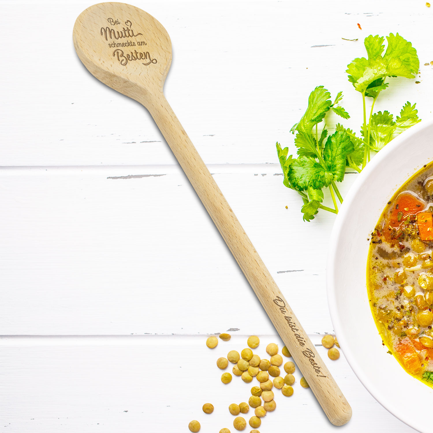 Heller Holzlöffel mit Gravur auf hellem Hintergrund neben Kräutern und Suppe