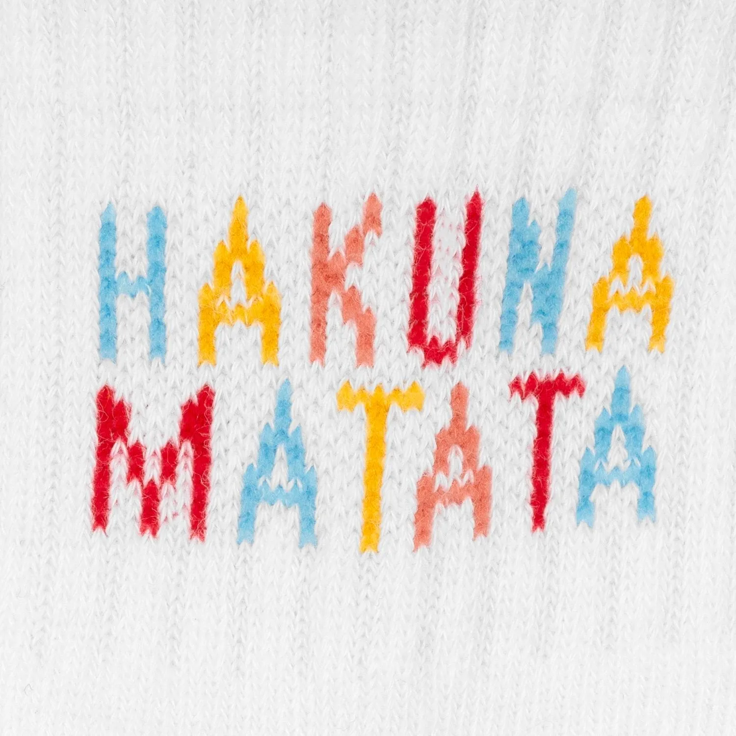 Weiße Baby-Zaubertennissocken mit buntem Hakuna Matata-Schriftzug auf gestricktem Stoff.