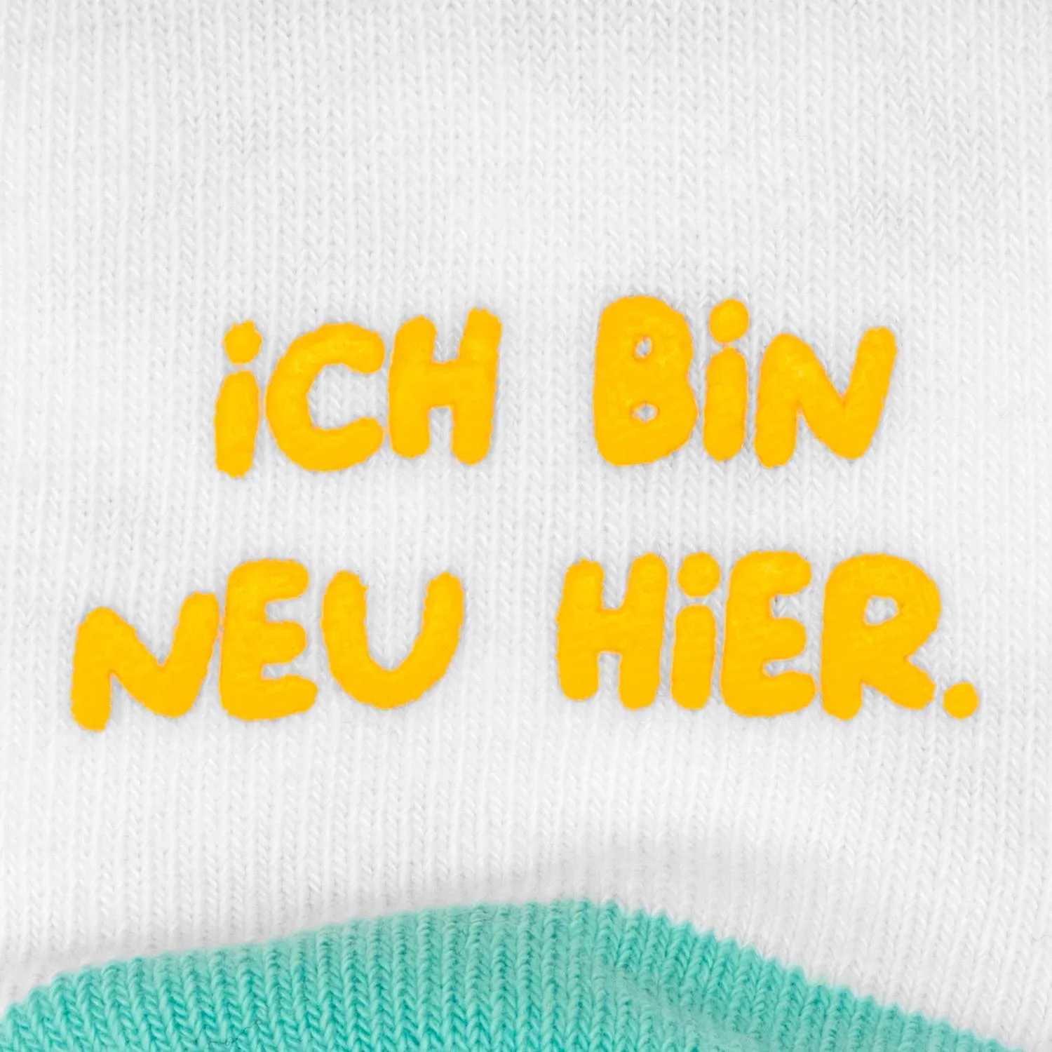 Weißes Strick-Sockenpaar mit orangefarbenem Schriftzug 'ich bin neu hier' und mintgrünem Rand.