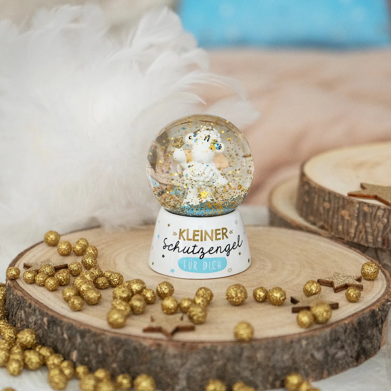 Schneekugel mit kleinem Schutzengel-Schaf, Goldsternchen und blauem Glitter auf weißem Sockel