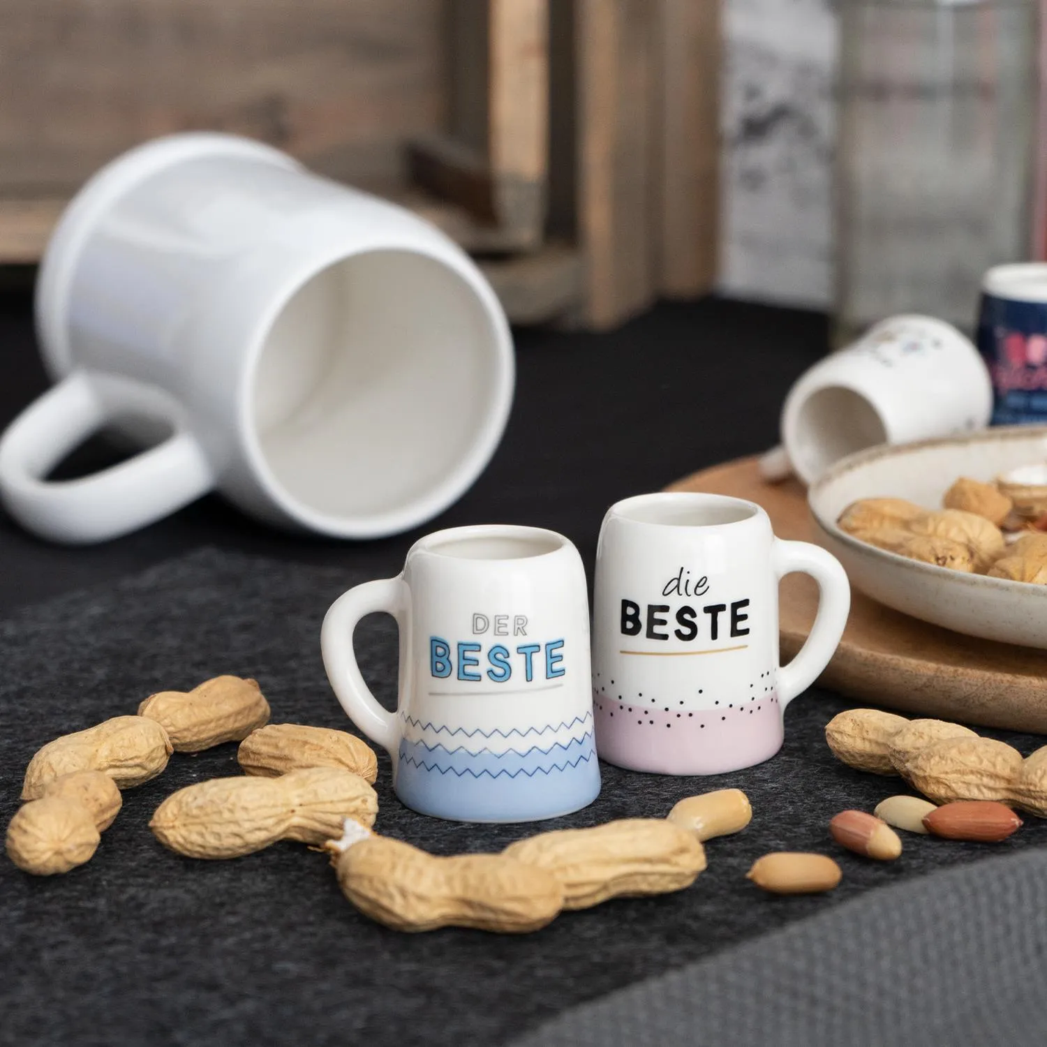 Zwei weiße Porzellan-Schnapsgläser mit blauer bzw. rosa Dekoration und Schriftzug.