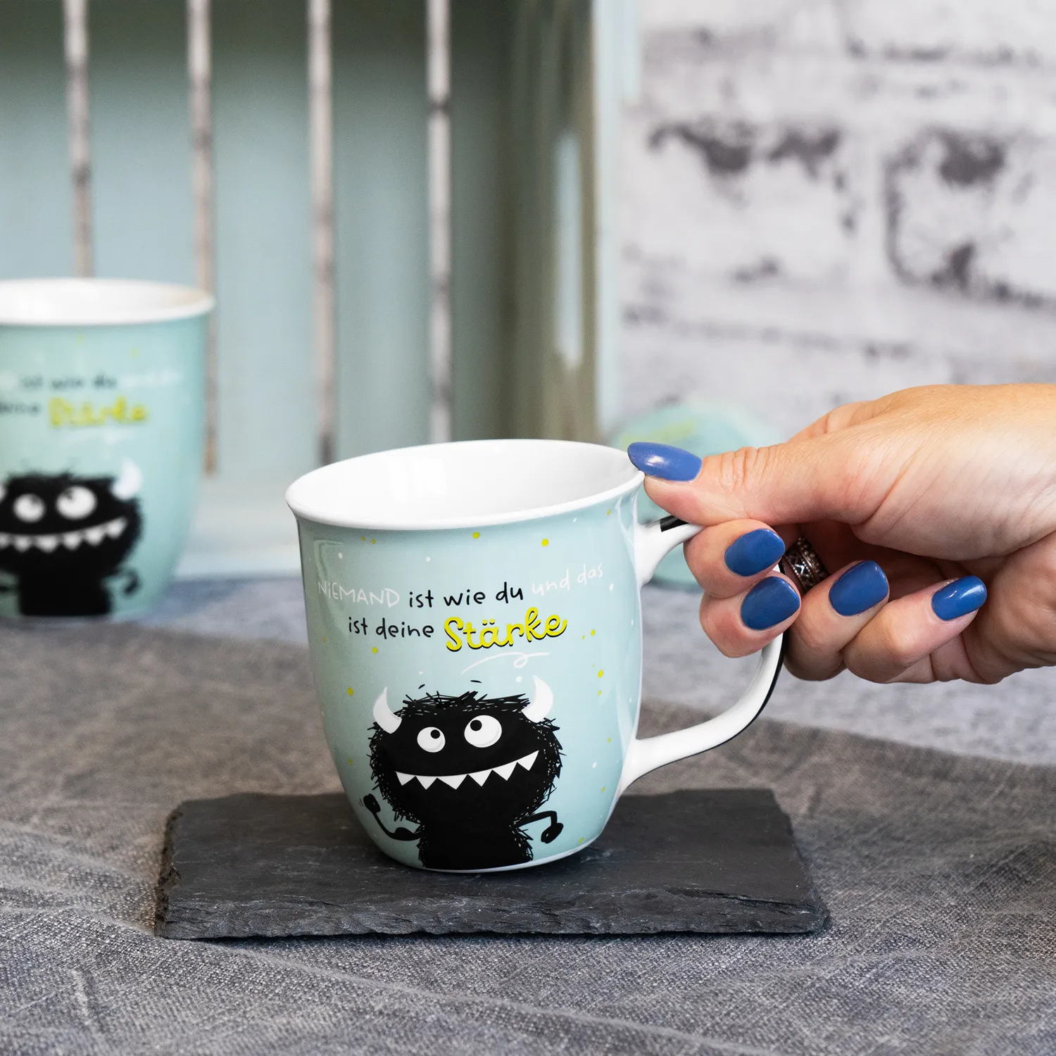 Pastell-türkisfarbene Porzellantasse mit schwarzem Monster-Motiv und Spruch.