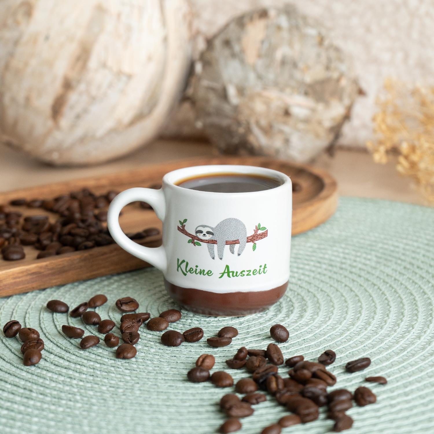 Weiße Espressotasse mit Faultier-Motiv auf Ast und braunem Bodenrand.