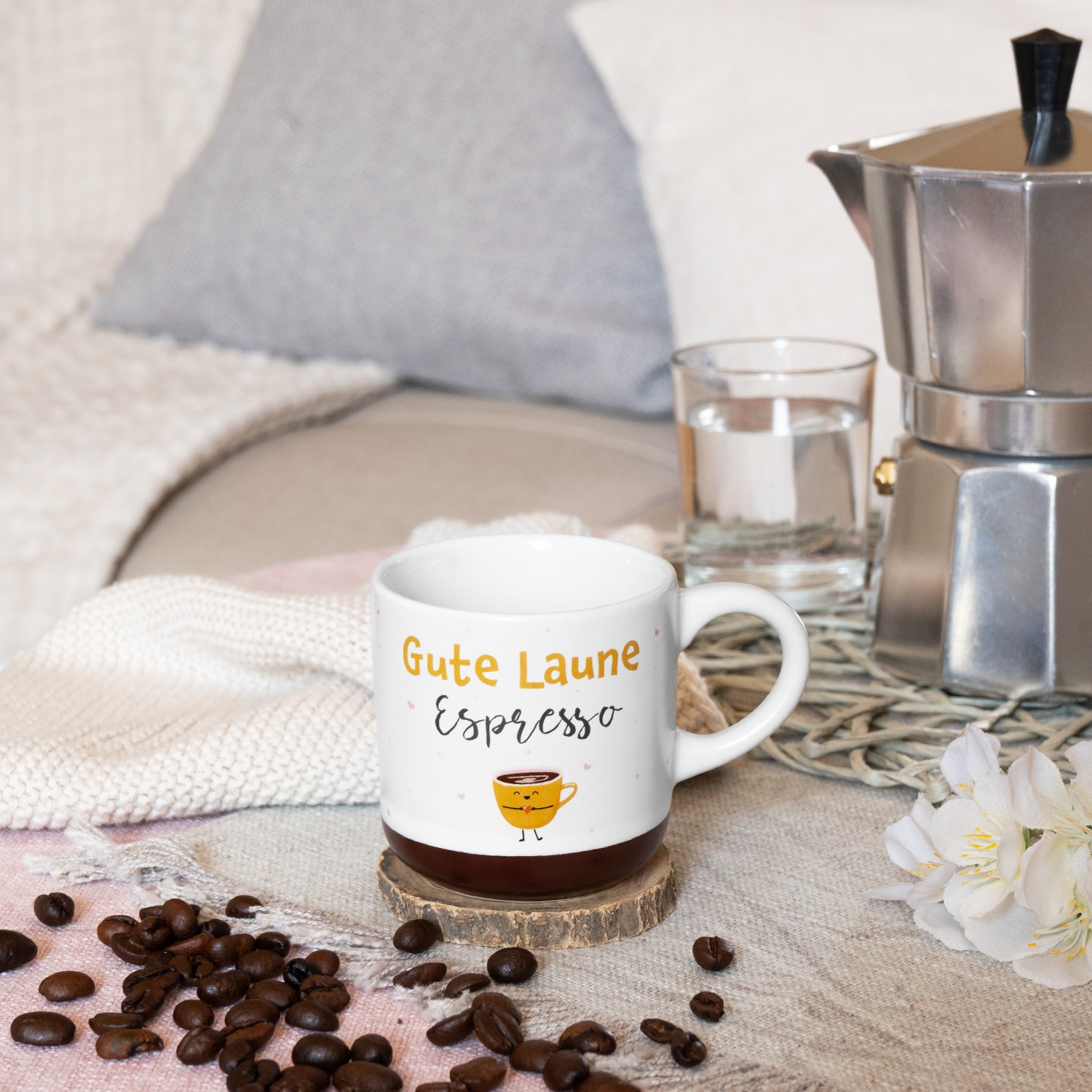 Weiße Espressotasse mit gelb-oranger Aufschrift 'Gute Laune Espresso' und braunem Boden auf Holzuntersetzer