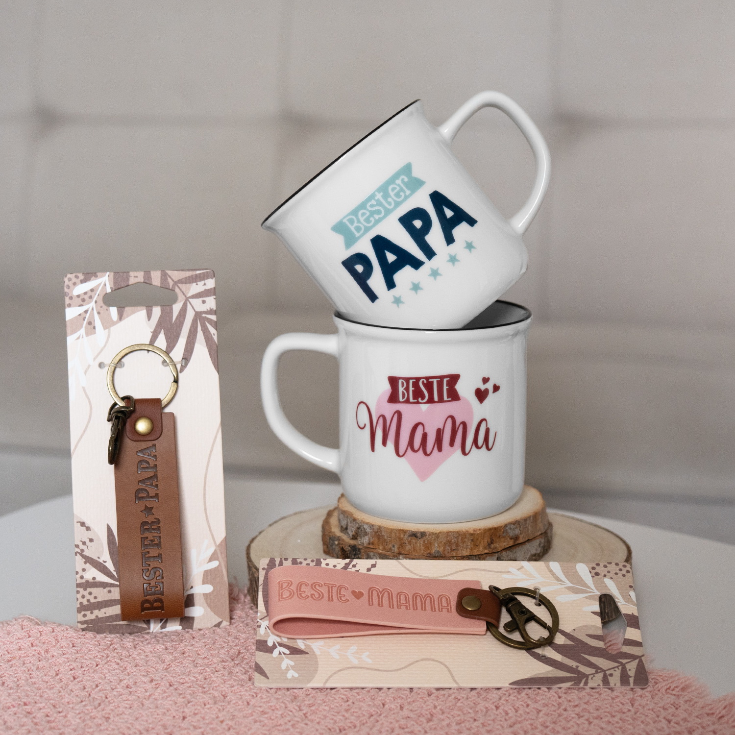 Zwei weiße Porzellan-Tassen mit Beste Mama und Bester Papa Motiv, ergänzt durch Schlüsselanhänger – liebevolles Geschenkset.