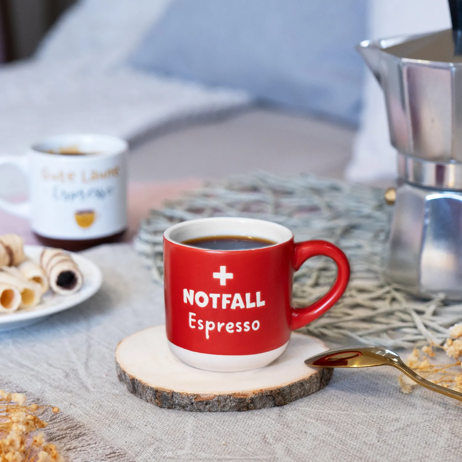 Rote Espressotasse mit weißem Schriftzug Notfall Espresso, auf Holz-Untersetzer.