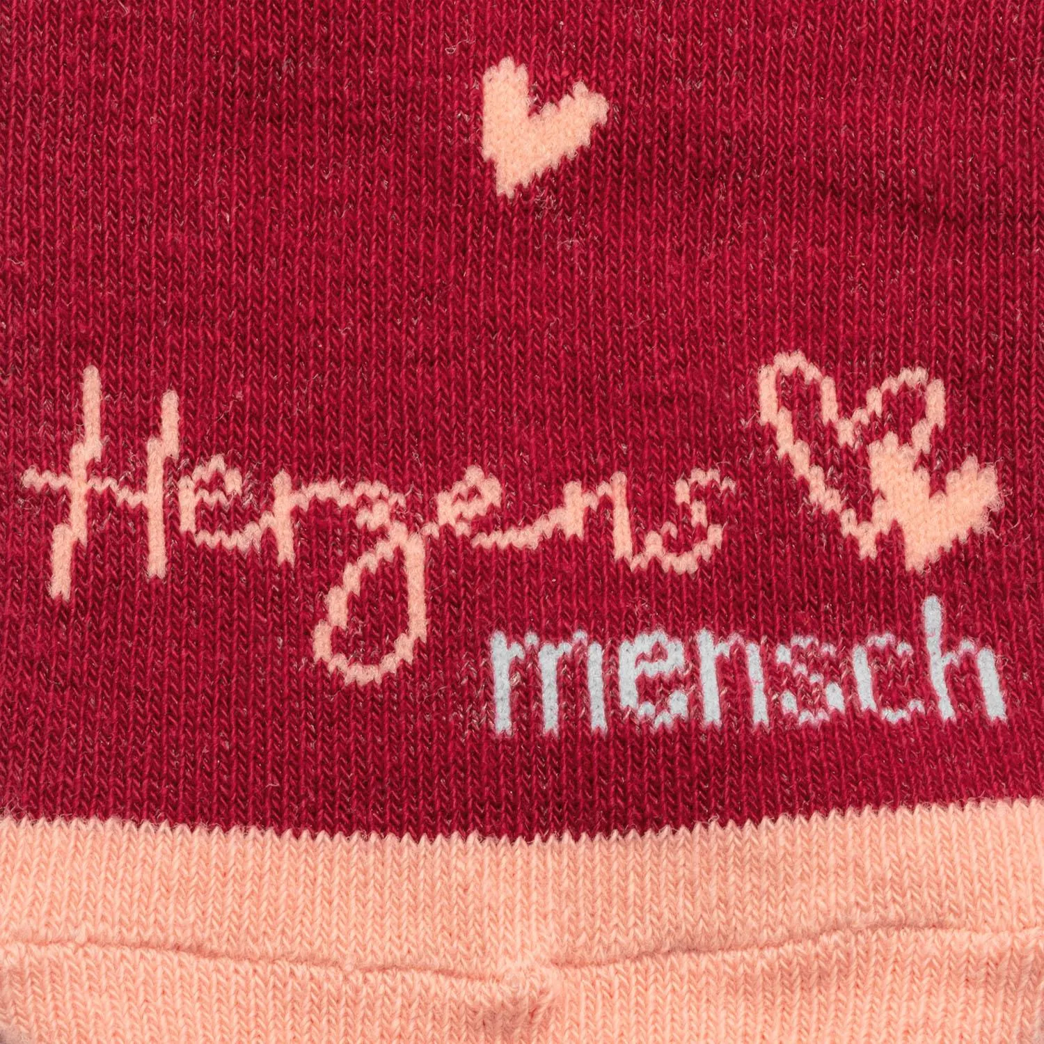 Rote Socke mit hellrosa Schriftzug 'herzens' und rosa Bündchen