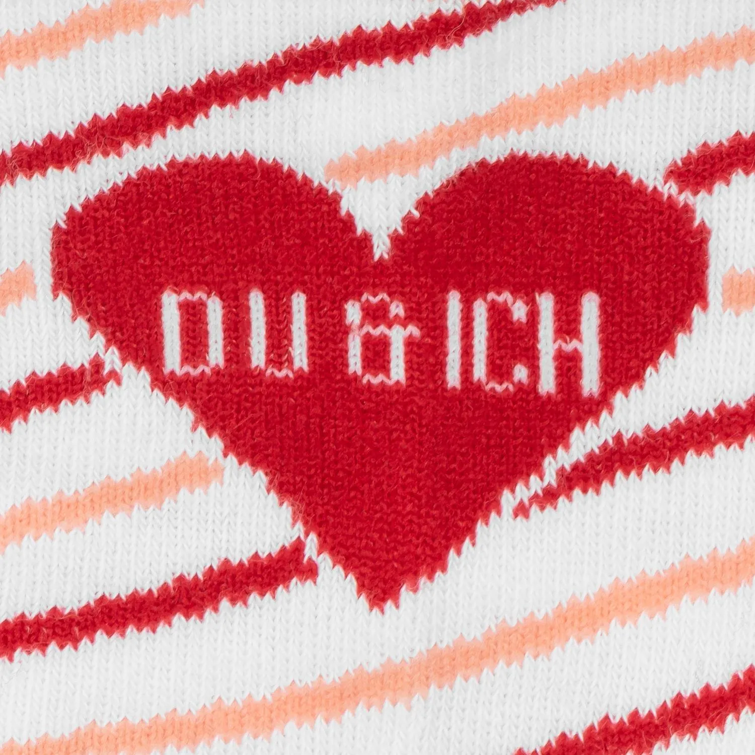 Weiße Socke mit rotem Herzmotiv und Schriftzug 'Du & Ich' vor Streifenmuster in Rosa und Orange
