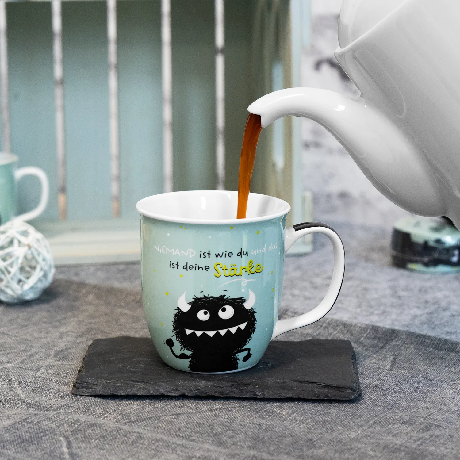 Pastellblaue Porzellan-Tasse mit Monster-Motiv und gelbem Spruch
