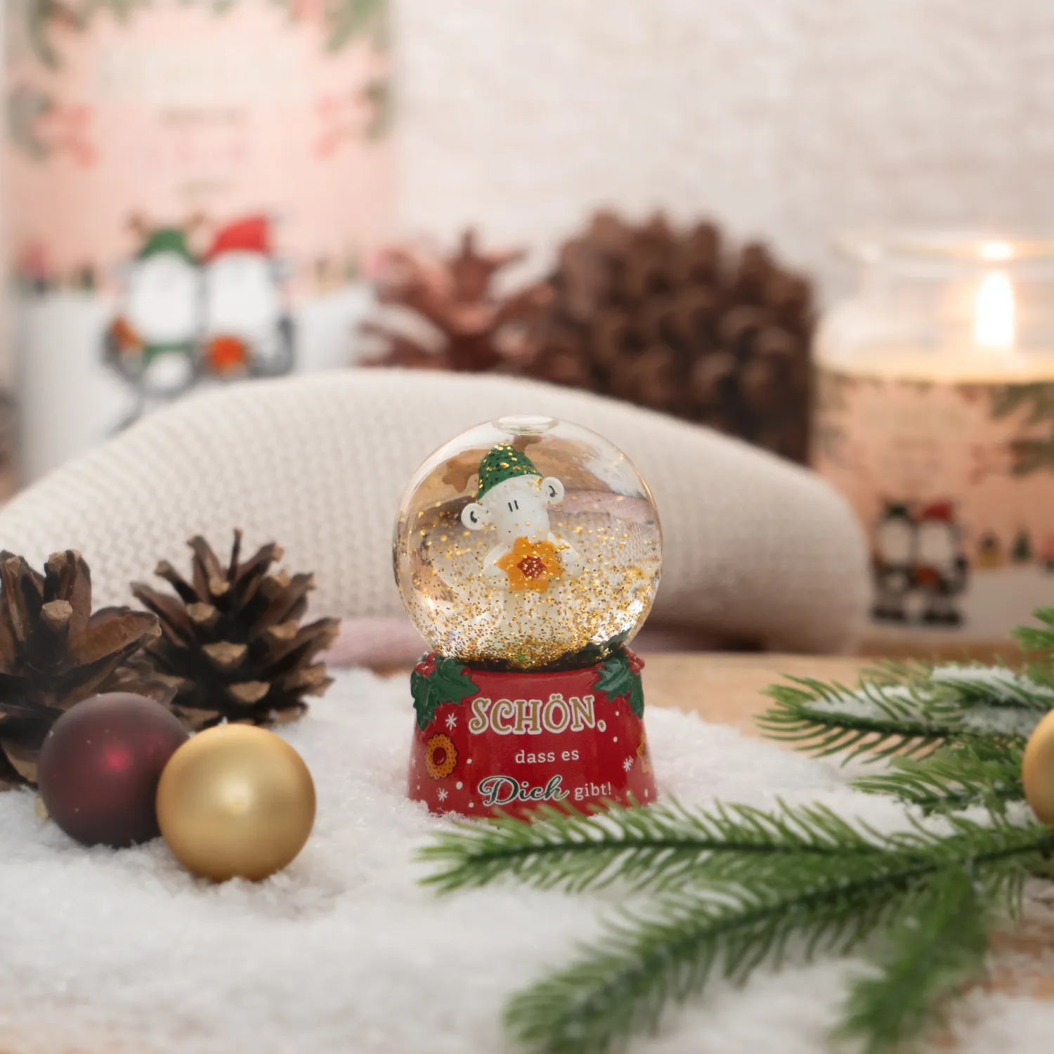 Schneekugel aus Glas mit weißer Tierfigur in grüner Mütze auf rotem Sockel