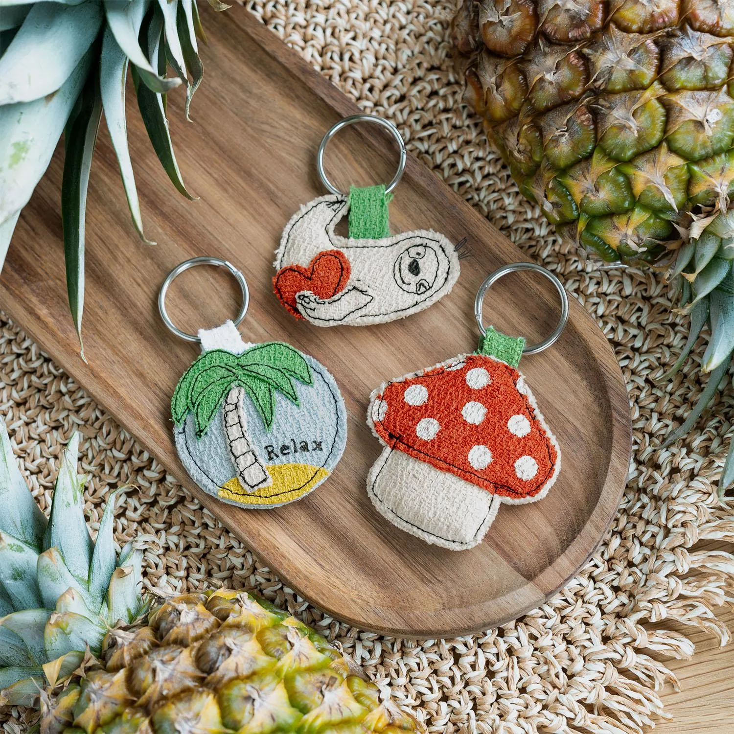 Drei niedliche Schlüsselanhänger aus Stoff mit Urlaubsmotiven: Palme, Pilz und Relax-Design auf Naturstoffen.