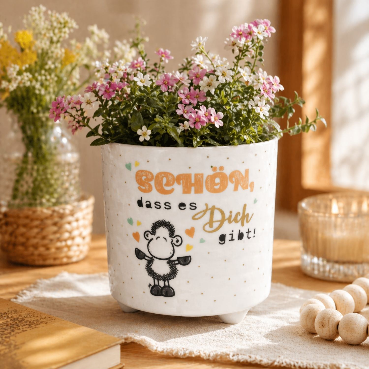 Weißer Blumenübertopf mit Schaf-Motiv und Golddruck, pink-weiße Blüten.