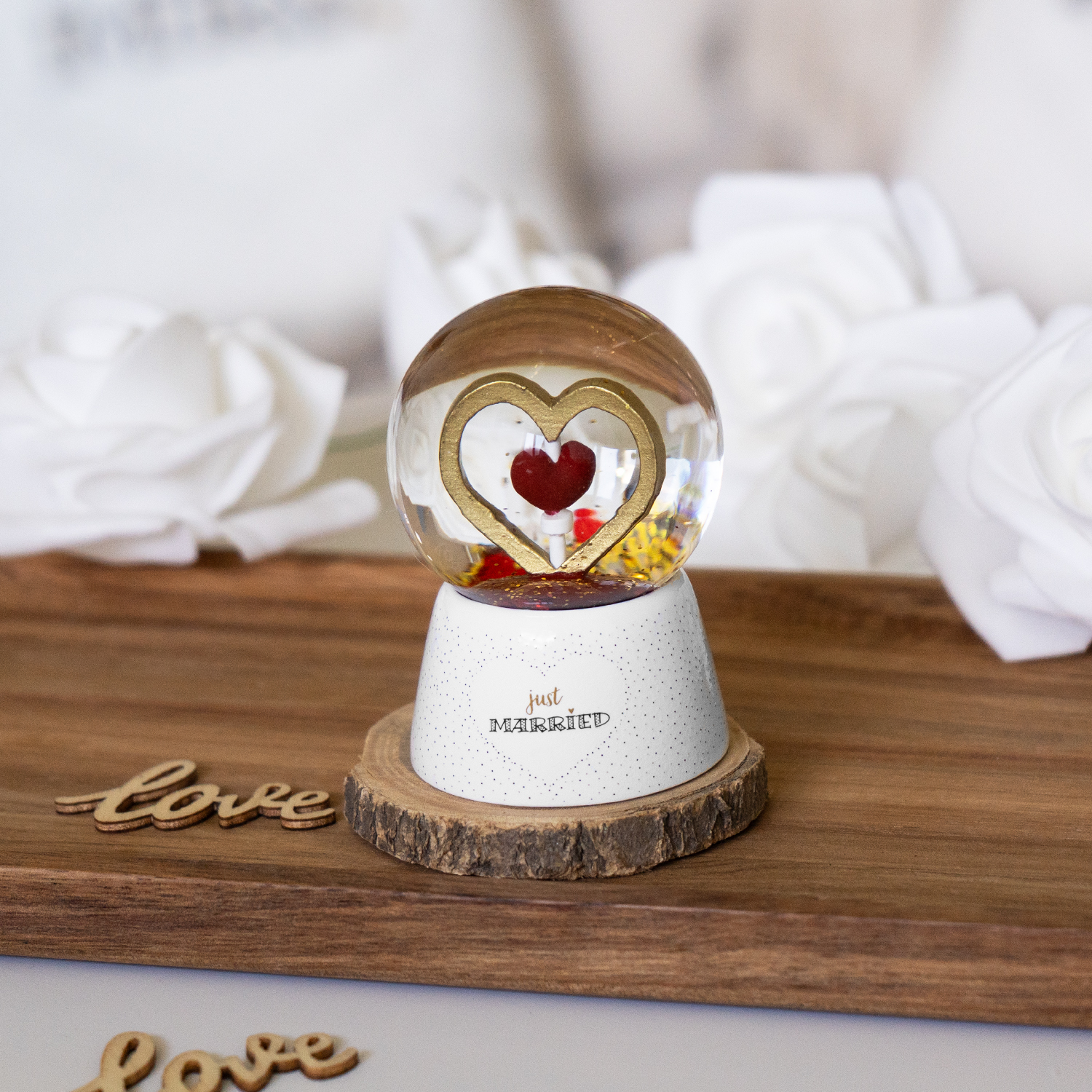 Gläserne Traumkugel mit goldenem Herzrahmen und rotem Glitzer auf weißem Sockel