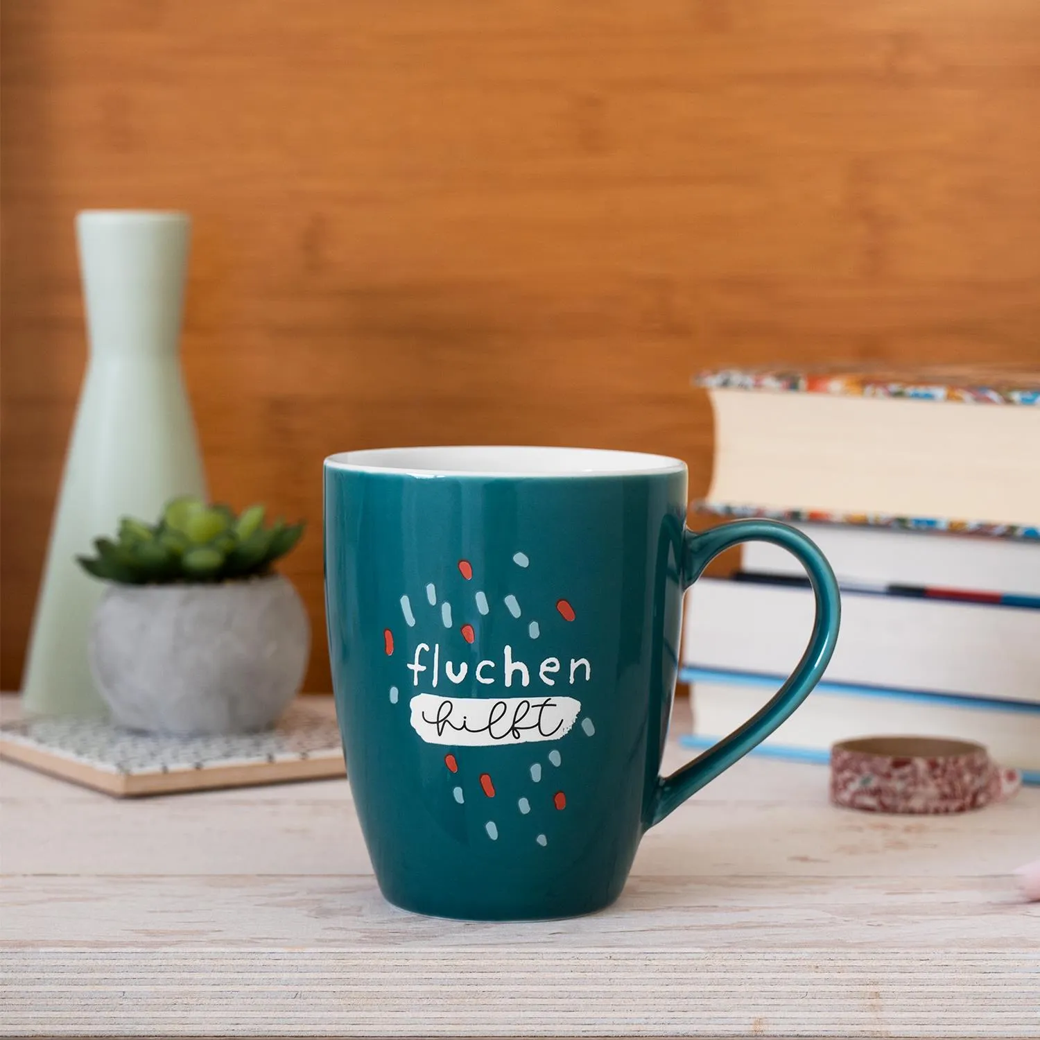 Tealfarbener Porzellan-Becher mit Schriftzug 'fluchen hilft' und bunten Sprenkeln