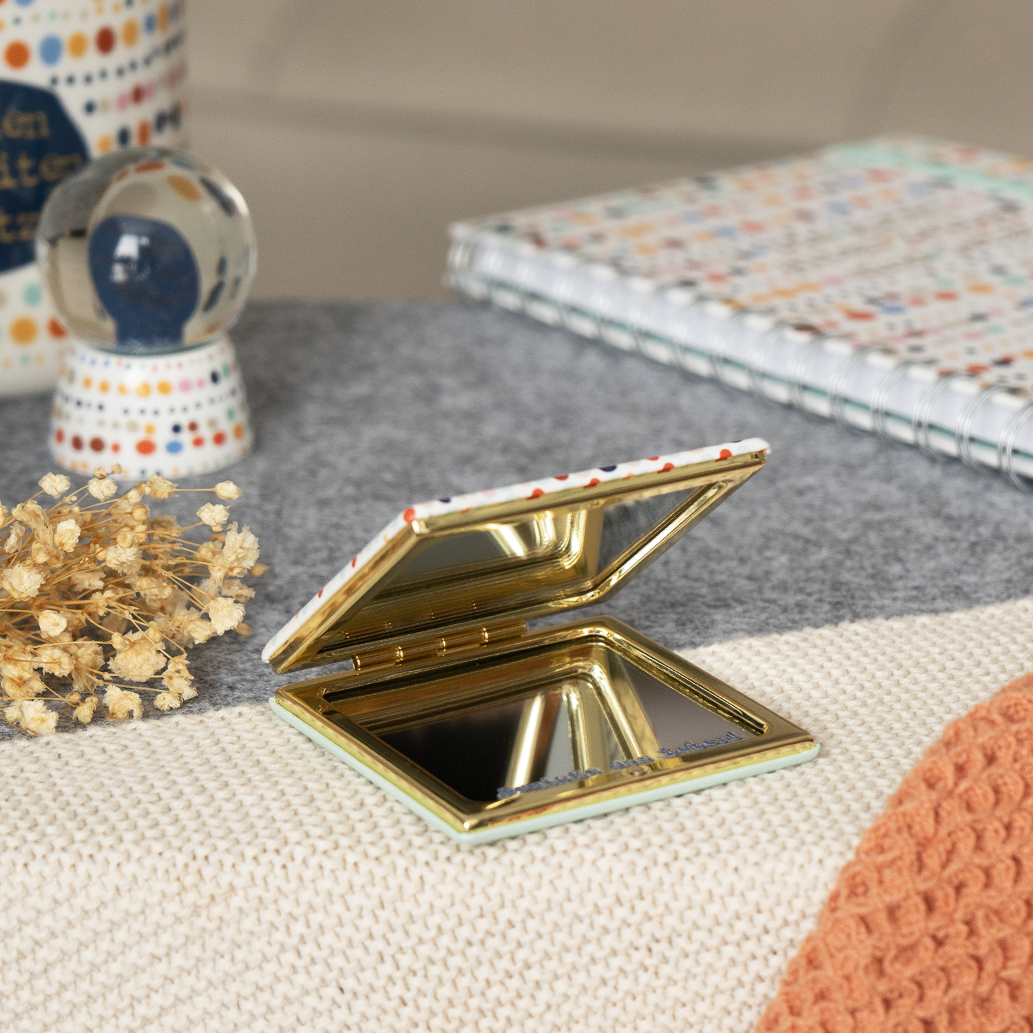 Kleiner Taschenspiegel mit buntem Punktemuster und goldener Innenfläche.