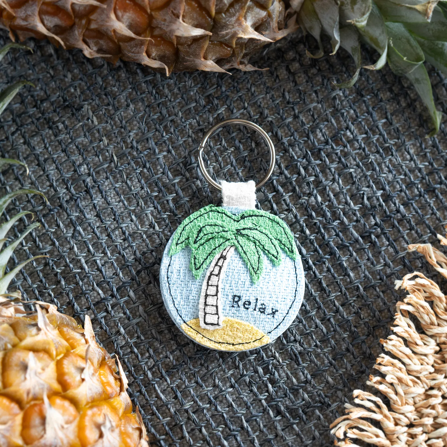 Runder Stoff-Schlüsselanhänger mit Palme, Insel und Relax-Schriftzug in Blau, Grün und Gelb
