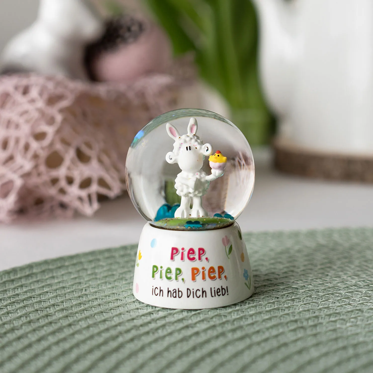 Schneekugel mit weißem Schaf-Figur in Glaskugel auf pastellfarbener Base