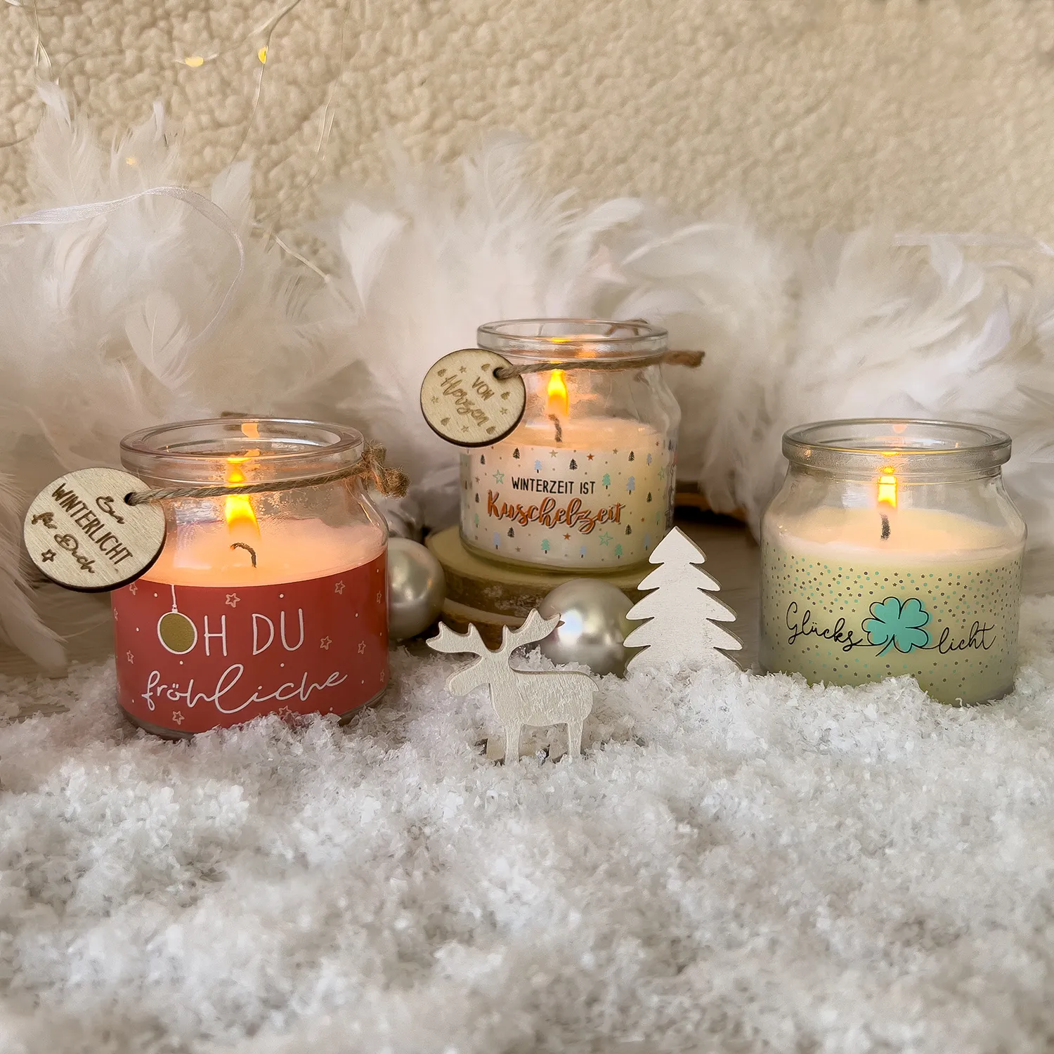 Drei Kerzengläser mit weißen Kerzen und farbigen Etiketten, Holzanhänger.