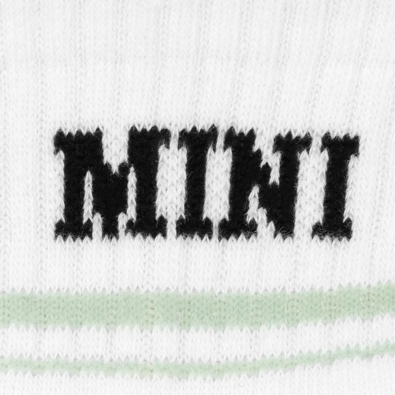 Weißes Baby-Zaubertennissocken-Paar mit schwarzem MINI-Aufdruck und Pastellgrün-Streifen.