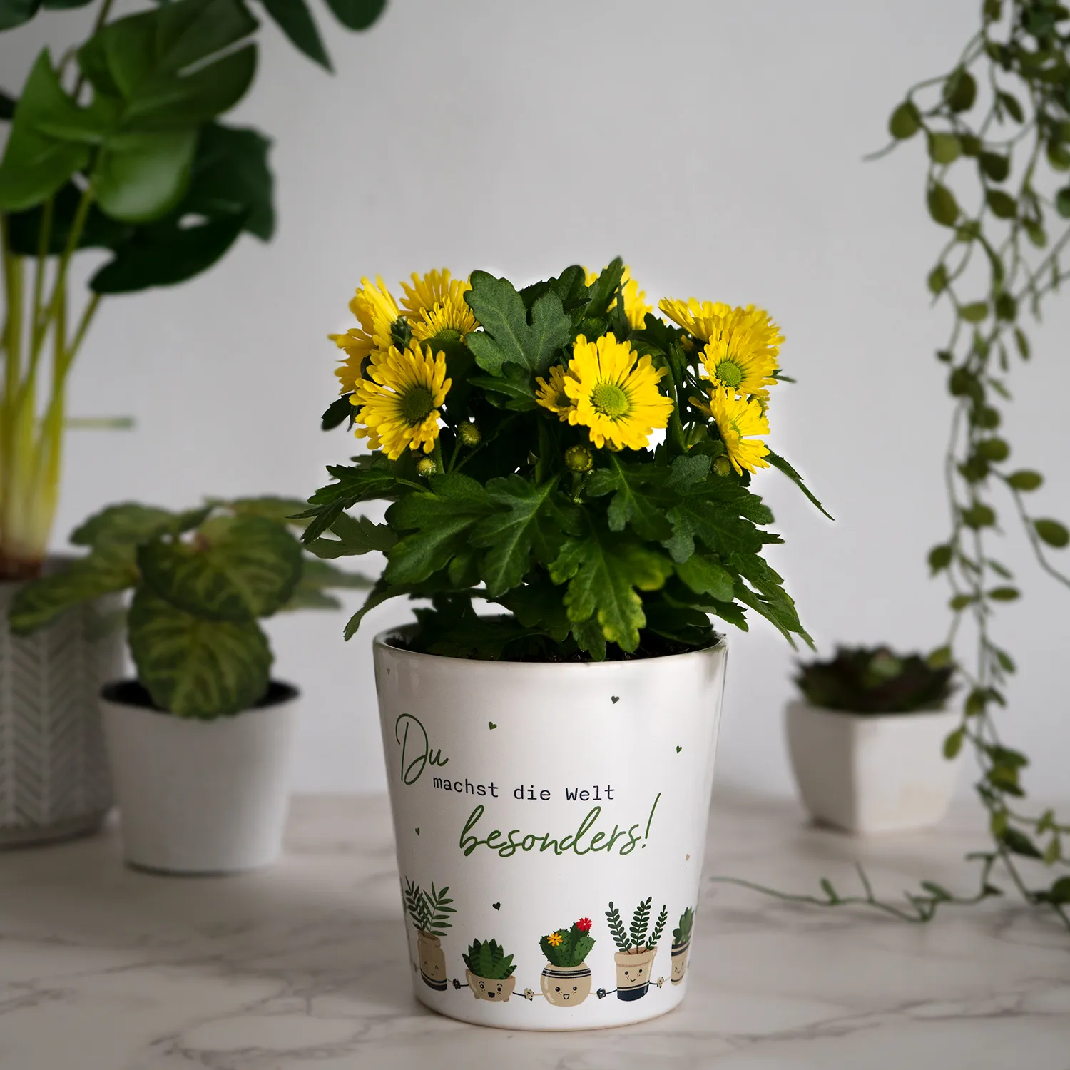 Weißer Keramik-Blumentopf mit gelben Blumen und grünem Laub – Motivdruck am Rand.
