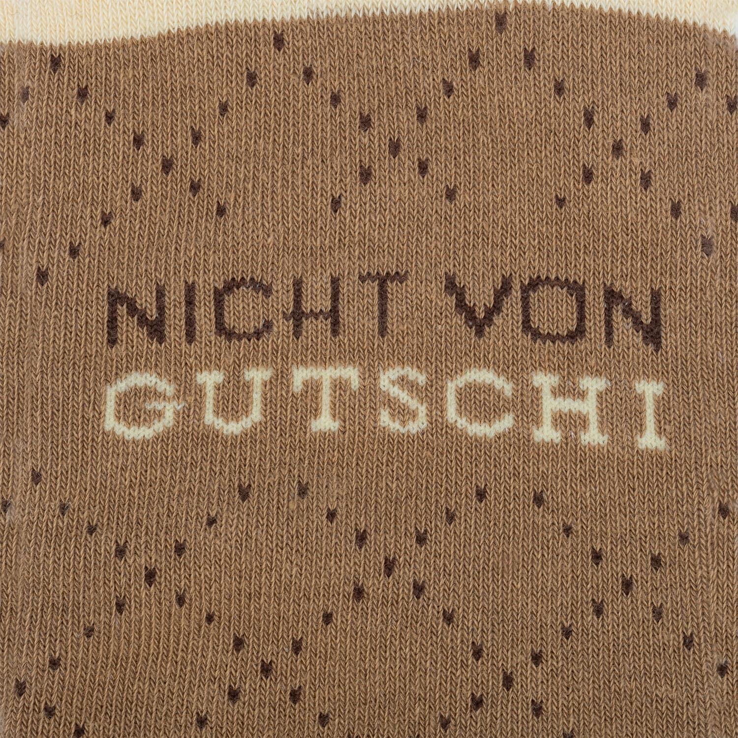 Braune Stricksocke mit hellem Schriftzug auf gestricktem Hintergrund