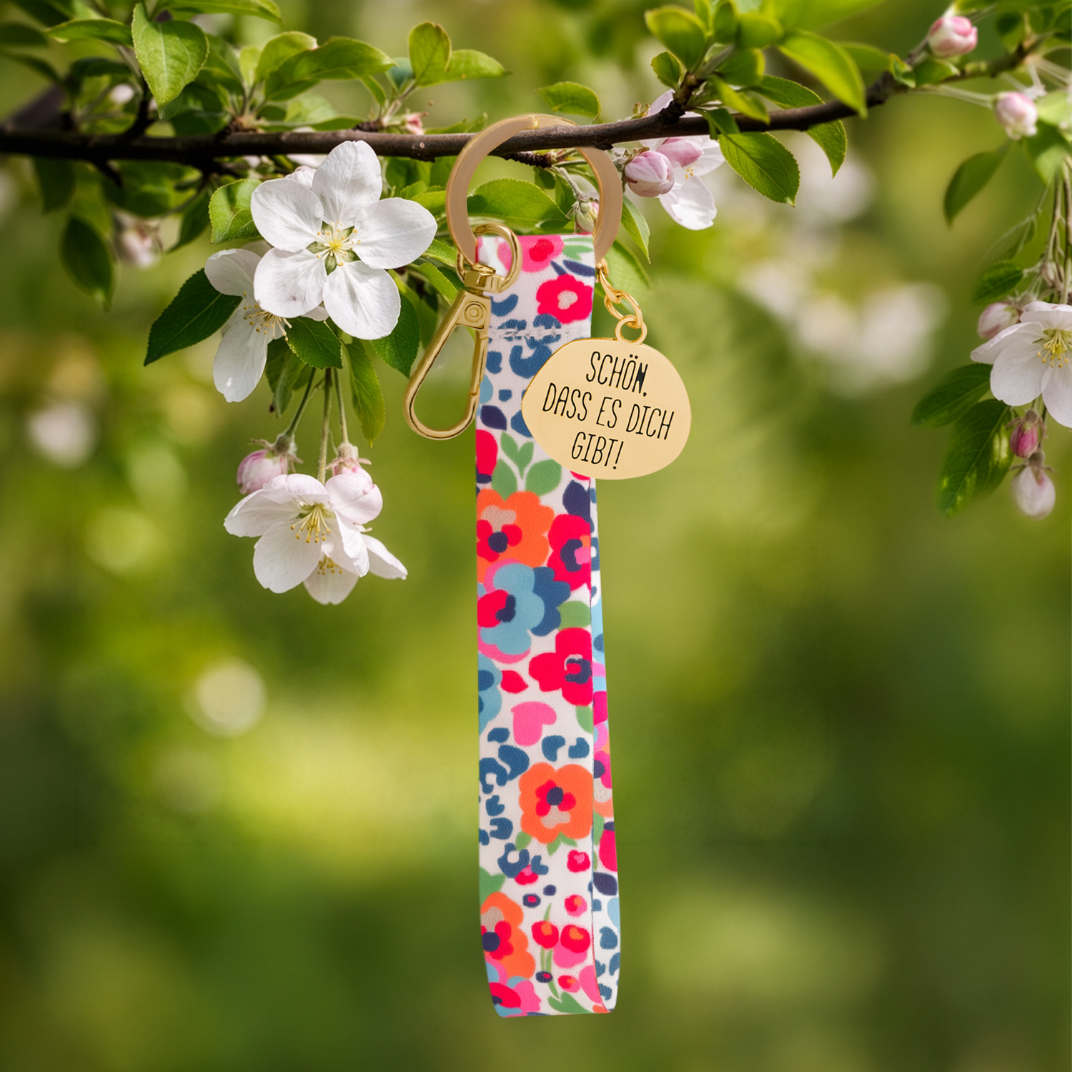 Floral gemustertes Schlüsselband mit goldenem Gravur-Anhänger vor Grün
